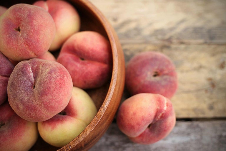 Drevená misa s plochými broskyňami na drevenom stole