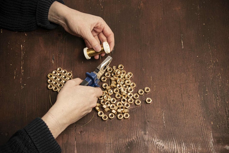 Osoba navlieka matice pomocou klieští a drôtu na drevený stôl