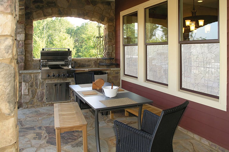 Krytá terasa s grilom, jedálenským stolom, stoličkami a drevenými lavicami.
