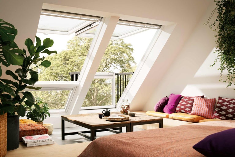 Podkrovná izba s oknami, dreveným stolom a vankúšmi vytvára svetlú a útulnú atmosféru.