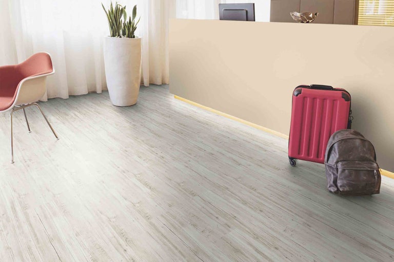 Svetlá miestnosť s laminátovou podlahou s dreveným vzhľadom, kreslom, kufrom a batohom