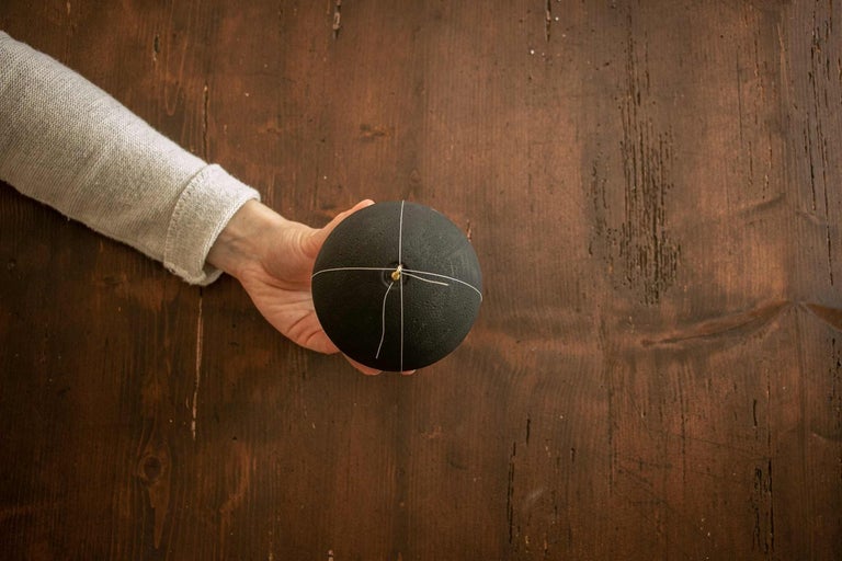 Ruka drží čiernu guľu so šnúrkou na drevenom stole