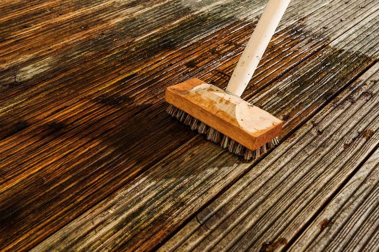 Drevená kefa čistí mokrú drevenú terasu.
