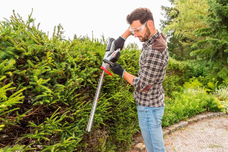 Muž strihá živý plot akumulátorovými nožnicami na živý plot v záhrade.