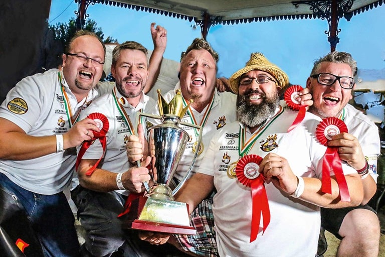 Skupina mužov oslavuje s trofejou a oceneniami