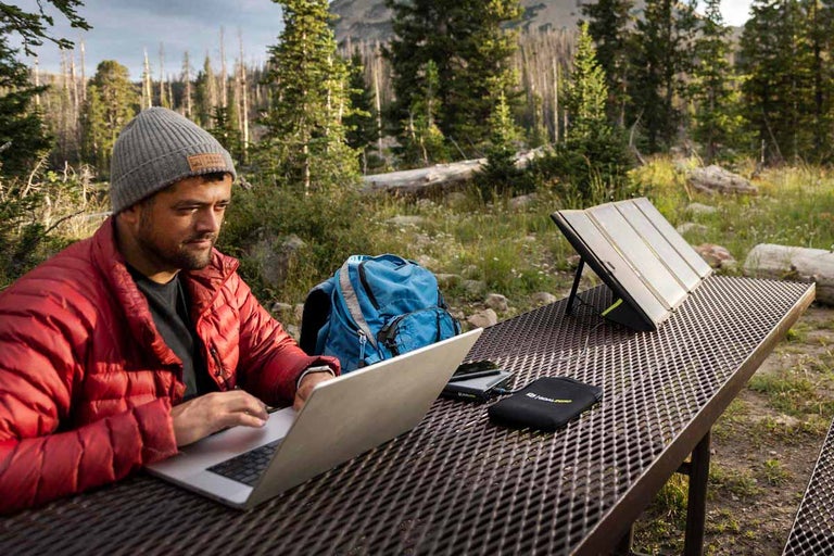 Muž s notebookom, solárnym modulom a batohom vonku