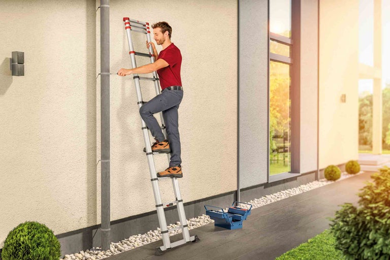 Muž na teleskopickom rebríku pracuje na stene domu s odkvapovou rúrou