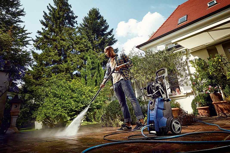 Muž čistí terasu vysokotlakovým čističom na záhrade.