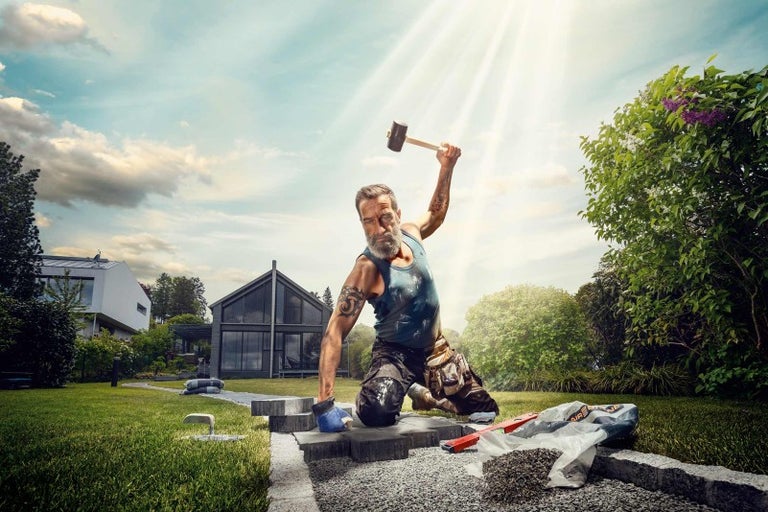 Muž kladie dlažobné kocky v záhrade s kladivom.