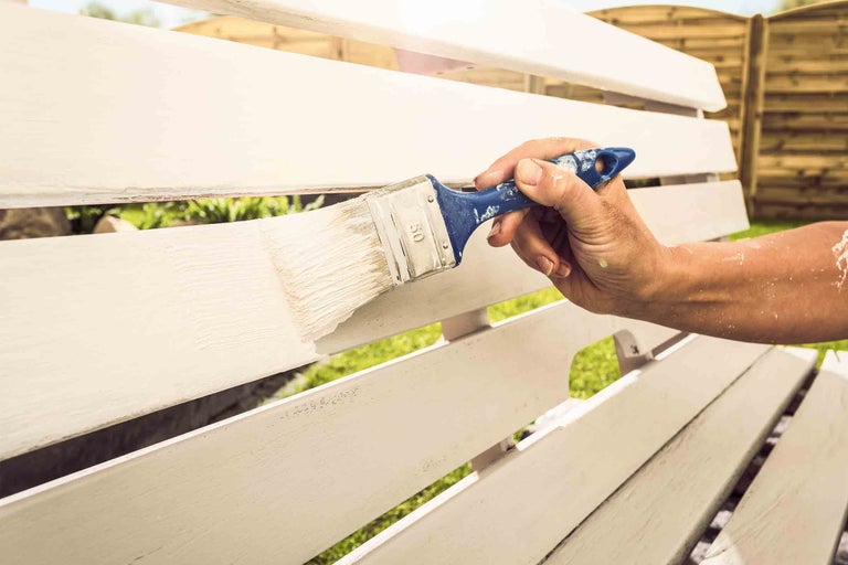 Osoba natiera záhradnú lavičku štetcom.