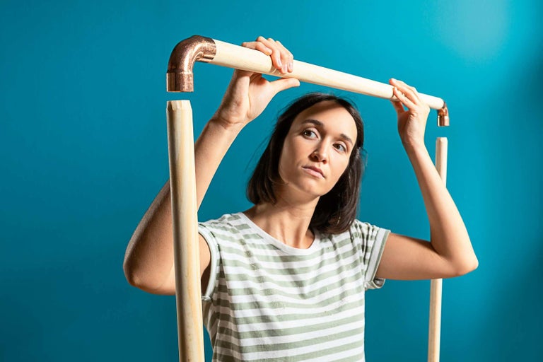 Žena montuje medenú rúrkovú spojku s drevenou tyčou