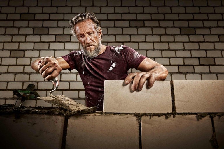 Muž muruje stenu z tehál a murárskej lyžice