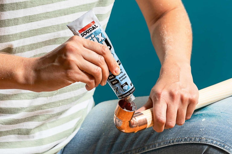 Osoba používa lepidlo z tuby na upevnenie medenej rúrky.