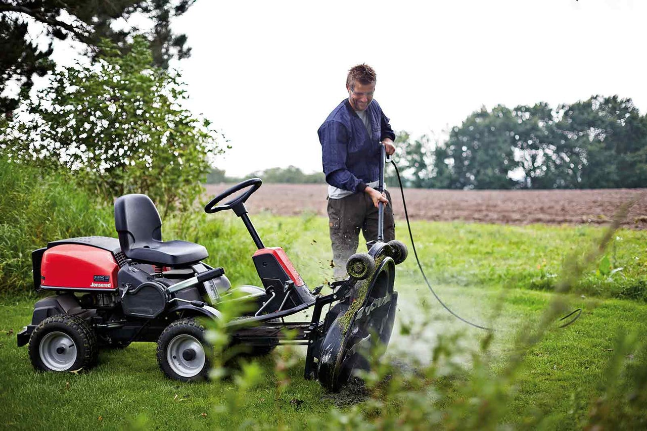 Muž čistí záhradný traktor Jonsered pomocou záhradnej hadice na trávniku.