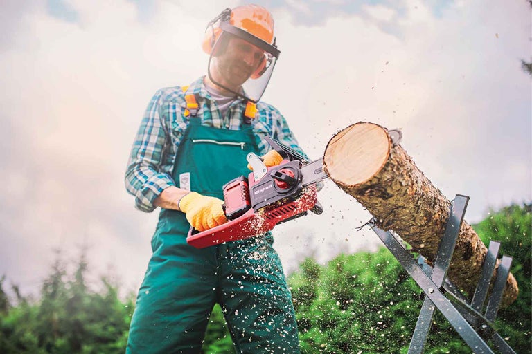Muž pília drevo elektrickou reťazovou pílou Einhell na kozovej píle.