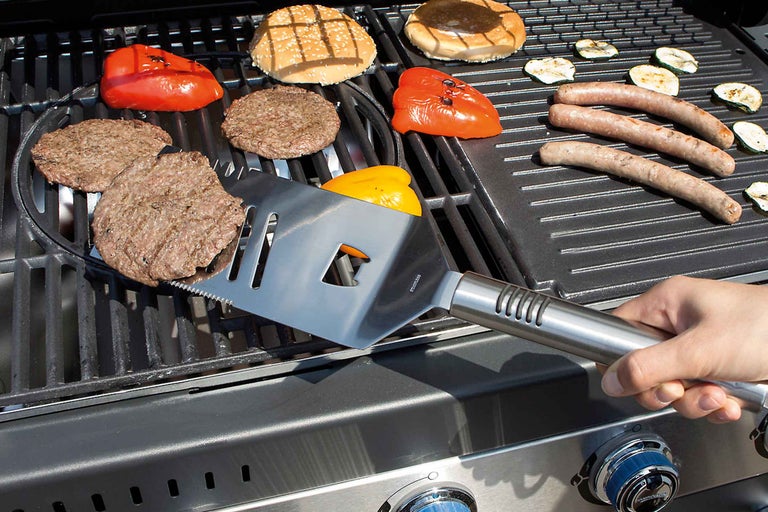 Grilovacia scéna s hamburgermi, paprikami, klobásami, cuketou a kovovou grilovacou lopatkou