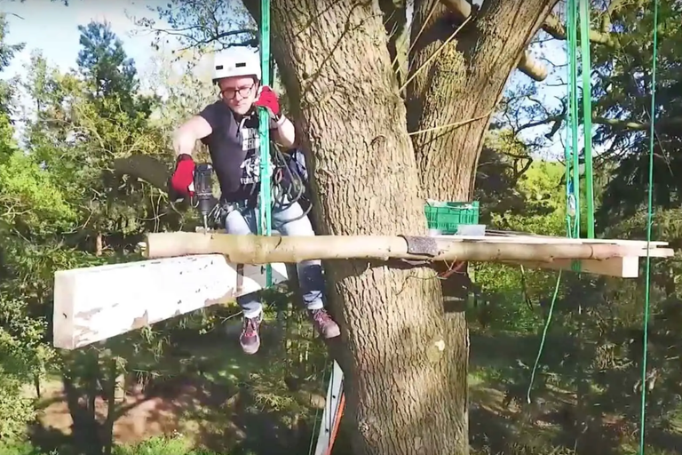 Muž s vŕtačkou stavia dom na strome na strome