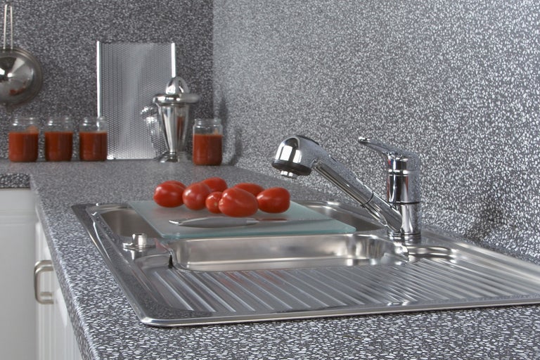 Nerezový kuchynský drez s batériou, doskou na krájanie a paradajkami na pracovnej doske