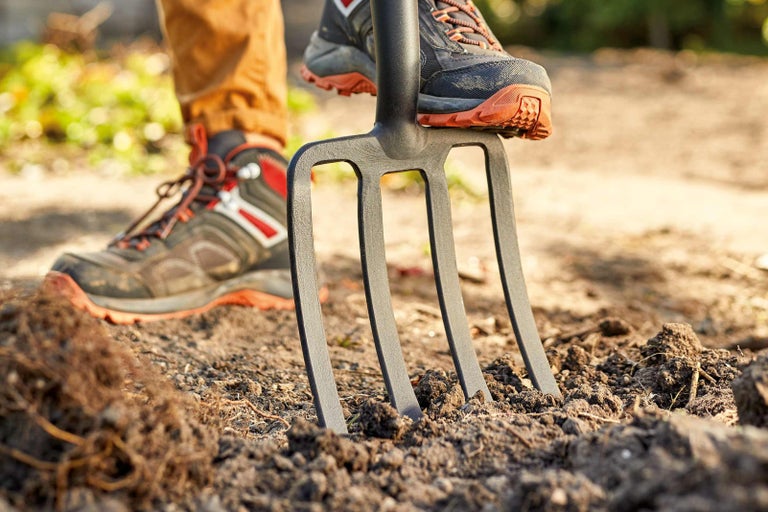 Detailný záber rýľovacích vidiel zatlačených nohou do zeme.