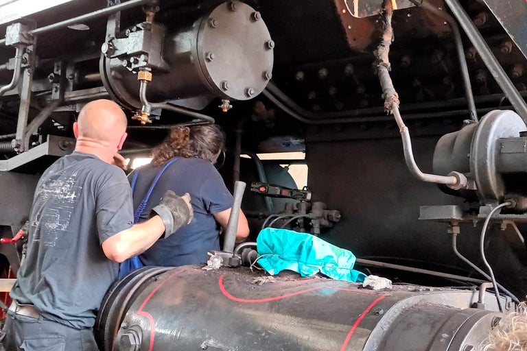 Interiér parnej lokomotívy s dvoma ľuďmi kontrolujúcimi mechaniku.