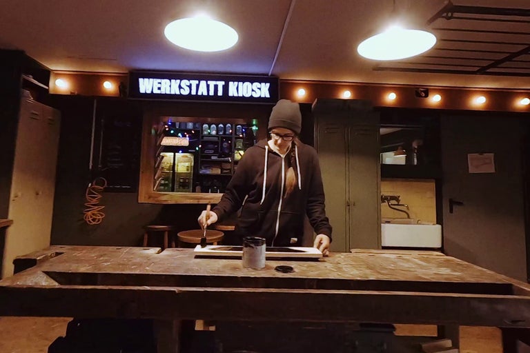 Žena natiera drevenú dosku štetcom na pracovnom stole v dielni