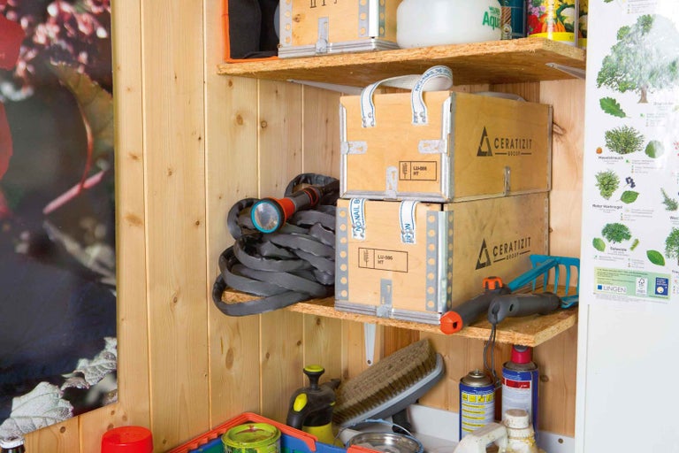 Polica s dvoma drevenými debnami, záhradnou hadicou a záhradným náradím.