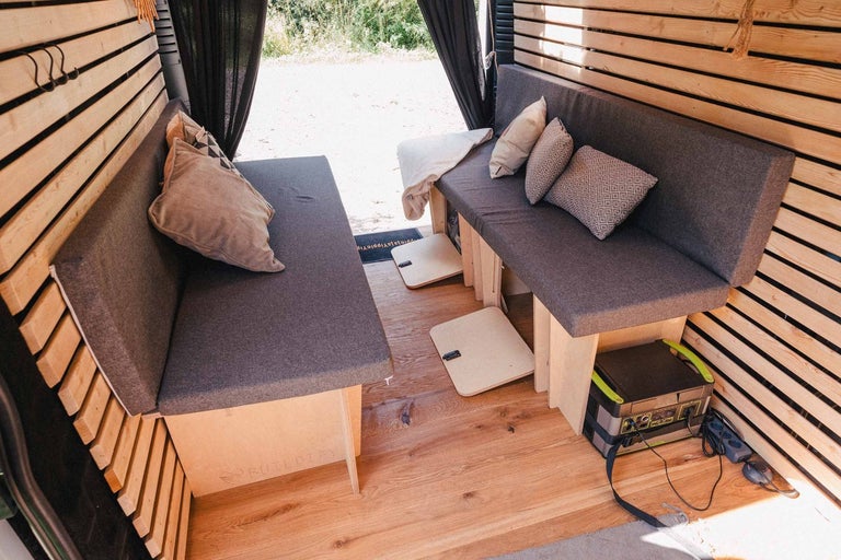 Interiér prestavanej dodávky s drevenými stenami, lavicami a vankúšmi.