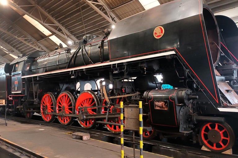 Čierna parná lokomotíva s červenými kolesami stojí v továrnej hale.