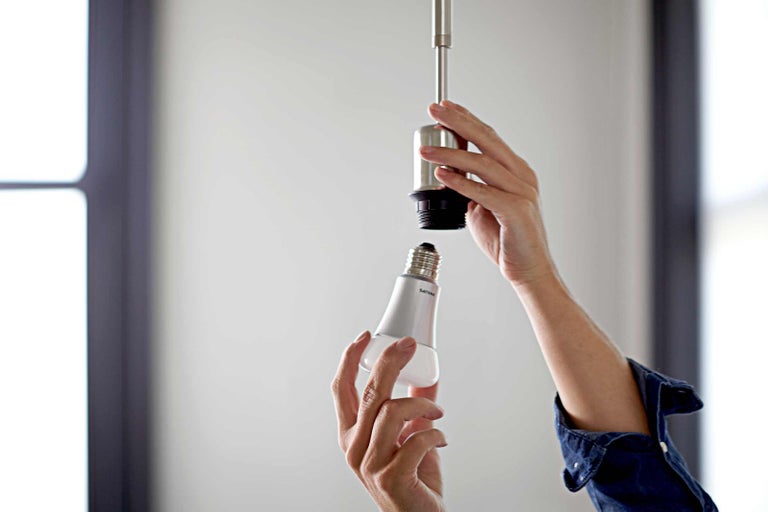 Osoba skrutkuje LED žiarovku do objímky.