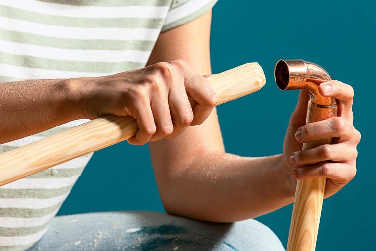 Osoba spája medenú rúrku s drevenou tyčou.