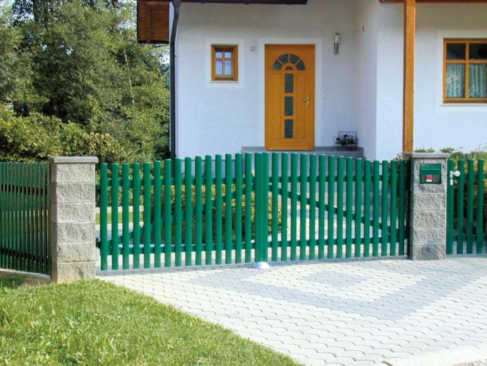 Zelený kovový plot s bránou pred obytným domom