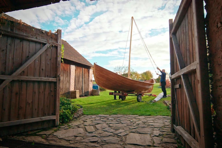 Drevená loď na prívese v záhrade s mužom pri stožiari