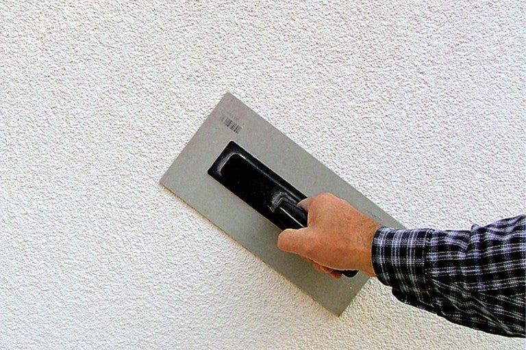 Remeselník omieta stenu ryhovanou omietkou a trecím doskou