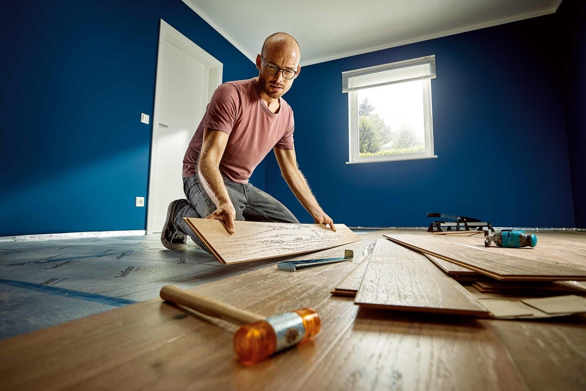 Muž pokladá laminátovú podlahu v miestnosti s náradím