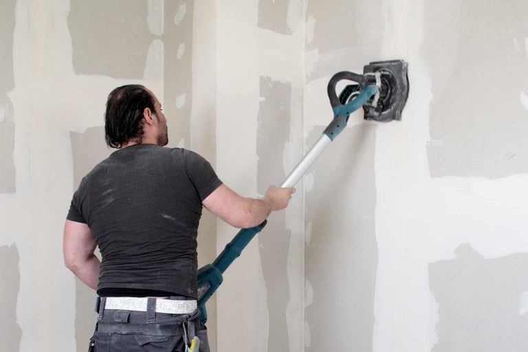Remeselník používa brúsku na sadrokartón na stenu na jej úpravu.