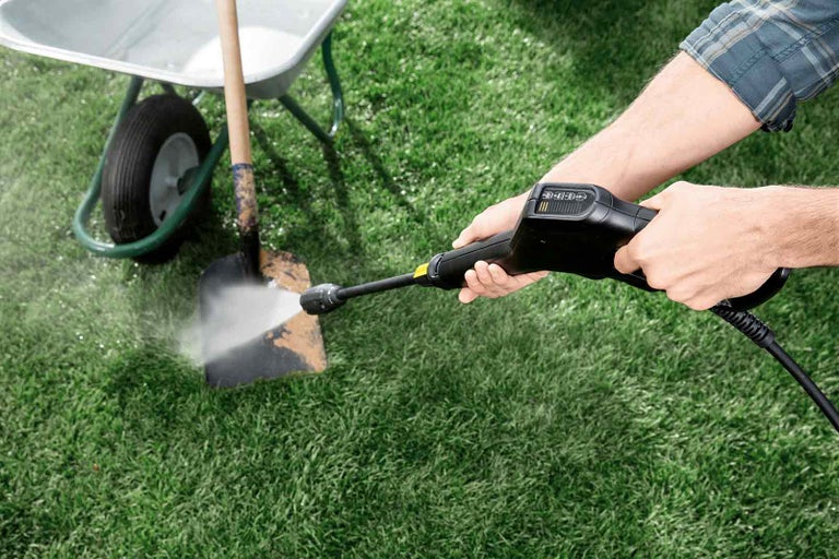 Osoba čistí lopatu vysokotlakovým čističom. V pozadí je vidieť koliesko a tráva.