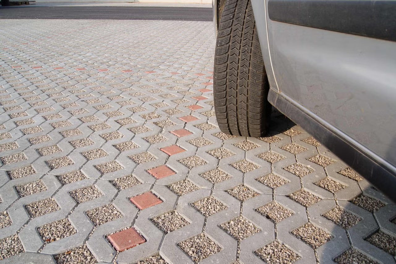 Auto na svetlom a organizovanom parkovisku z betónovej zatrávňovacej dlažby vyplnenej štrkom a červenými označovacími kameňmi.