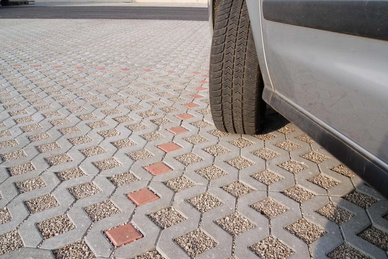 Auto na svetlom a organizovanom parkovisku z betónovej zatrávňovacej dlažby vyplnenej štrkom a červenými označovacími kameňmi.