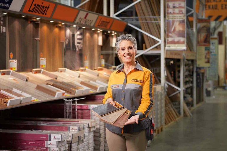Zamestnankyňa spoločnosti Hornbach prezentuje vzorky laminátu pred regálom s laminátom.
