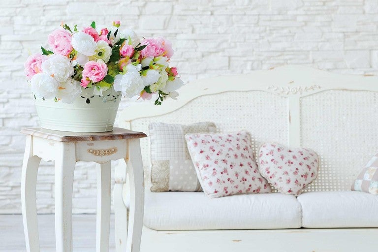 Dekoratívna scéna s kvetinovou väzbou v kovovom vedre na odkladacom stolíku vedľa lavice s vankúšmi.