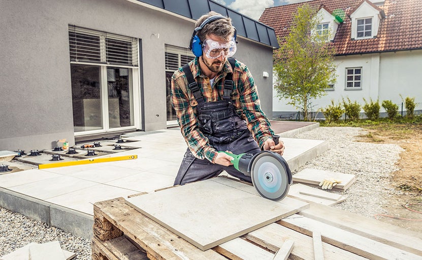 Muž vonku reže dlaždice pomocou brúsky