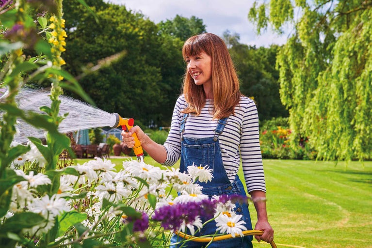 Žena zavlažuje kvety záhradnou hadicou a striekacou pištoľou