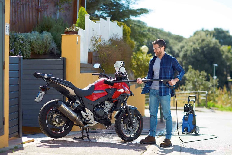Muž čistí motocykel vysokotlakovým čističom vonku.
