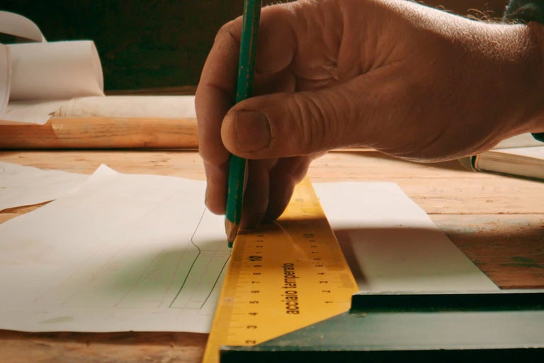 Osoba kreslí na papier ceruzkou a pravítkom.