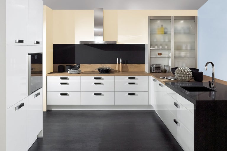 Moderná kuchyňa s bielymi skrinkami, čiernou pracovnou doskou a nerezovým odsávačom pár