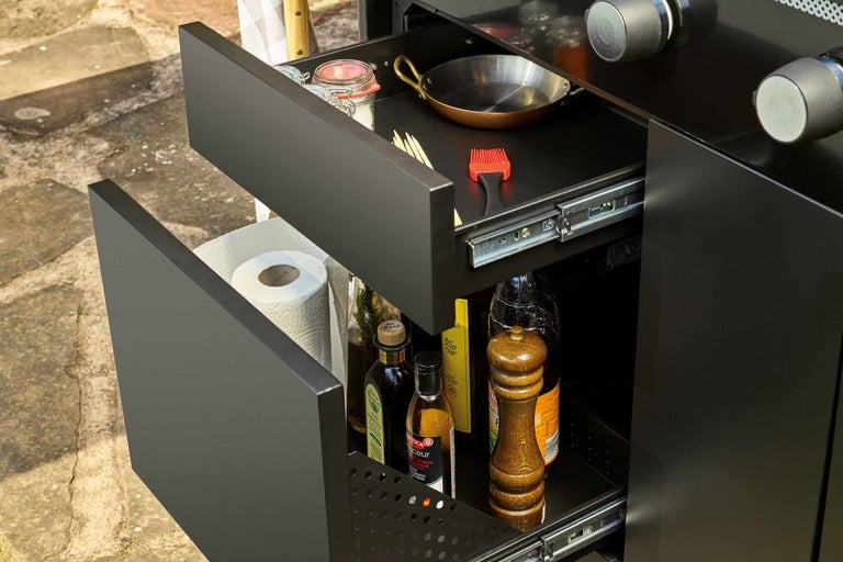 Čierna vonkajšia kuchyňa s dvoma otvorenými zásuvkami plnými kuchynského náčinia.