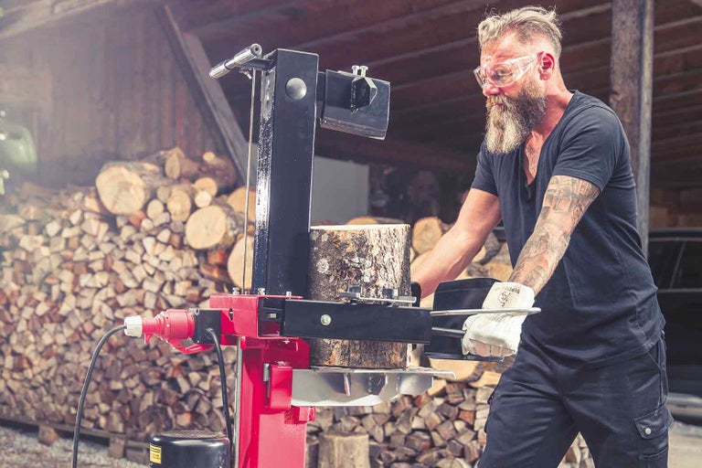 Muž štiepa drevo s elektrickou štiepačkou dreva pred hromadou dreva