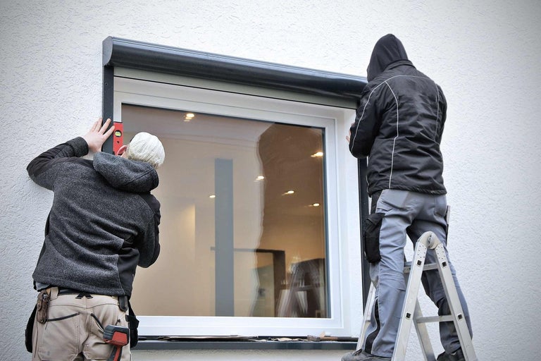 Dvaja remeselníci montujú roletu na okno.
