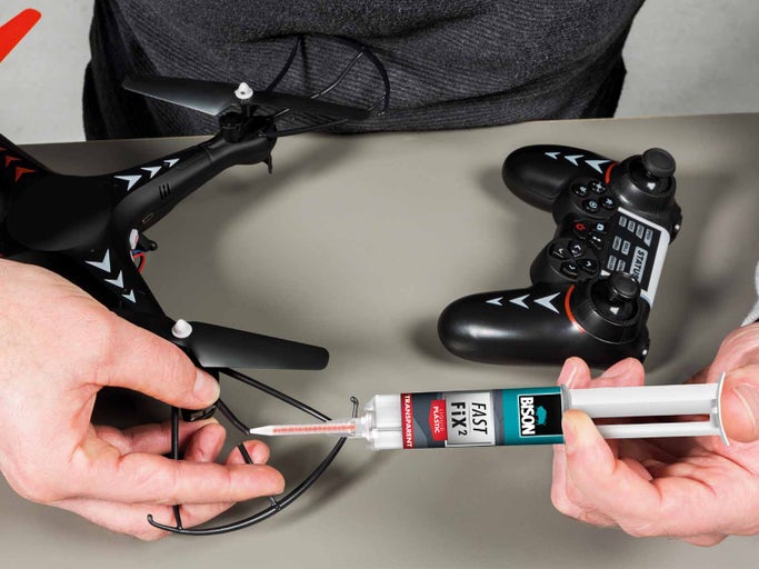 Osoba opravuje dron s lepidlom na plasty Bison vedľa diaľkového ovládania.