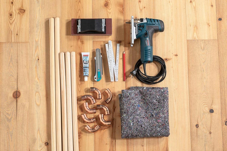 Drevené tyče, lepidlo, odlamovací nôž, skladací meter, ceruzka, priamočiara píla, medené kolená a zakrývacia plachta na drevenej podlahe